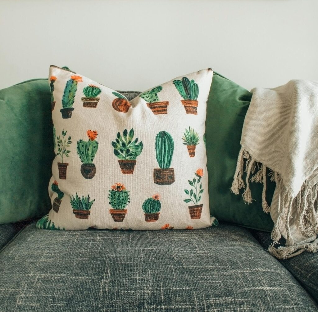 A modern living room with green cushions, cactus pillow, and cozy throw blanket on a sofa.