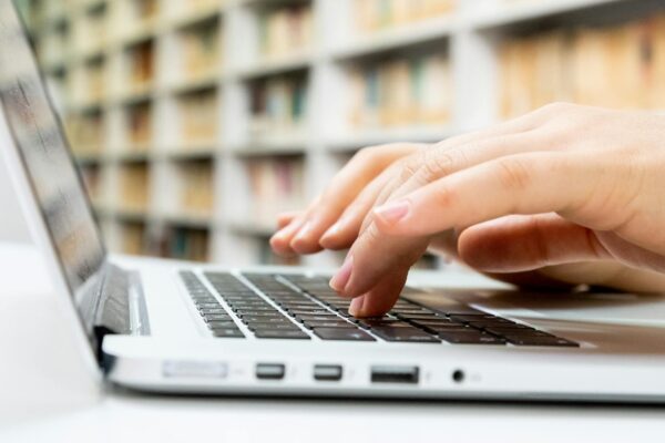 Close-up of hands typing on a laptop keyboard in a library setting.