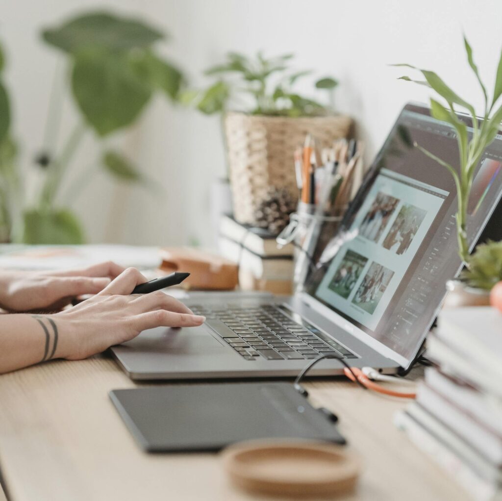 Freelance designer working from home using a laptop and digital tablet, surrounded by plants.