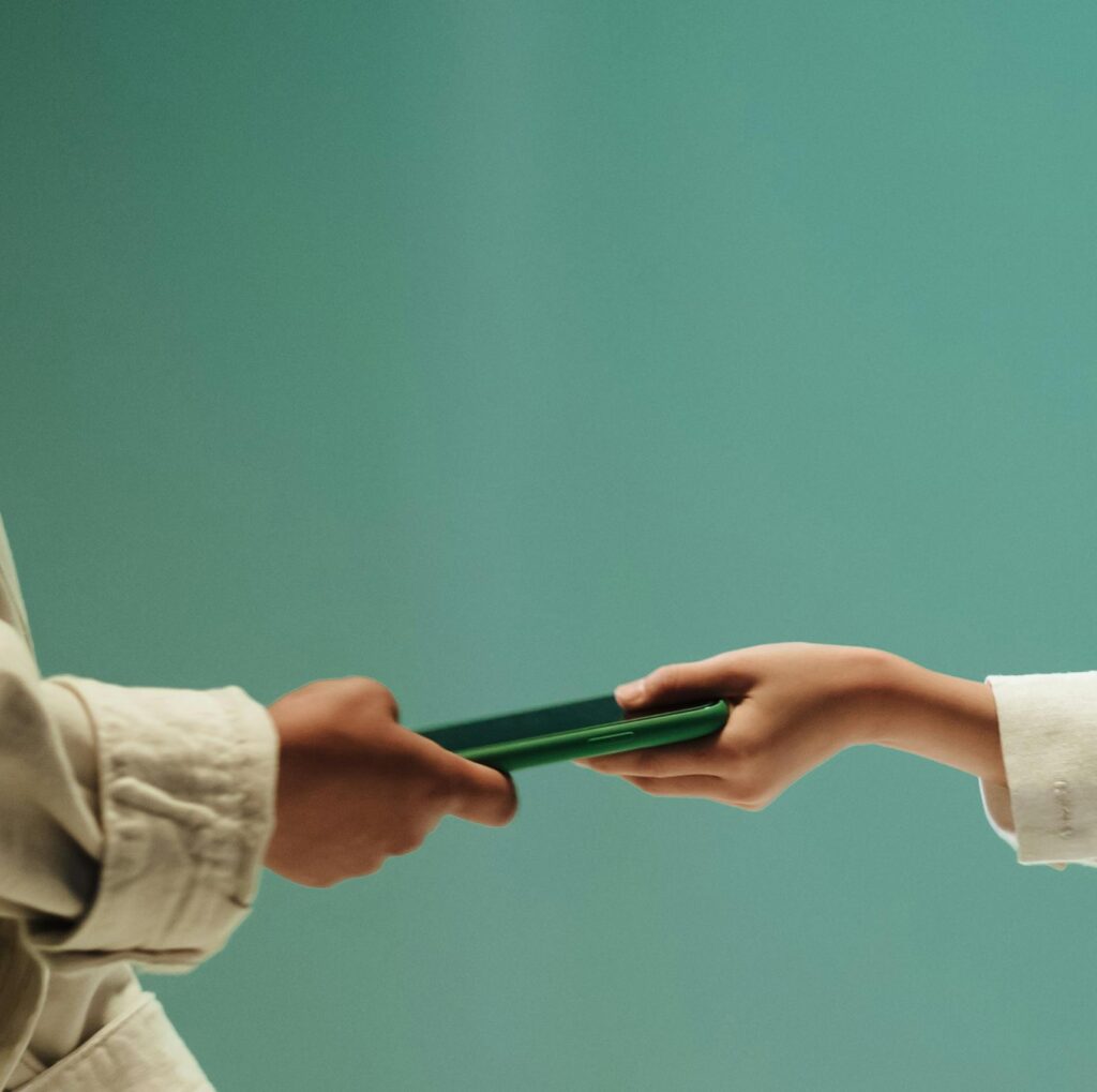 Two people exchanging a green mobile phone against a solid green background.
