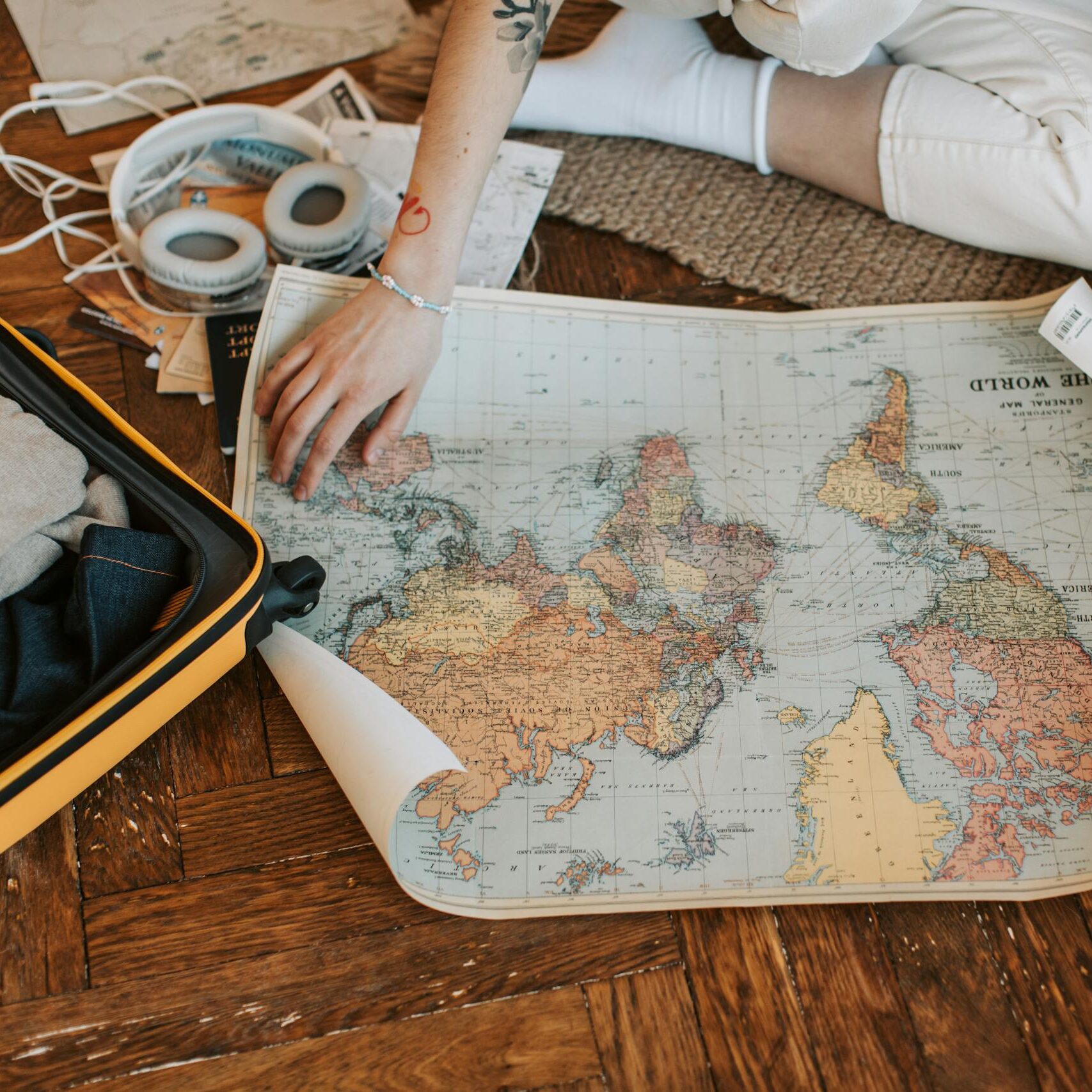 A traveler plans a journey, sitting on the floor with a world map and suitcase filled with essentials.