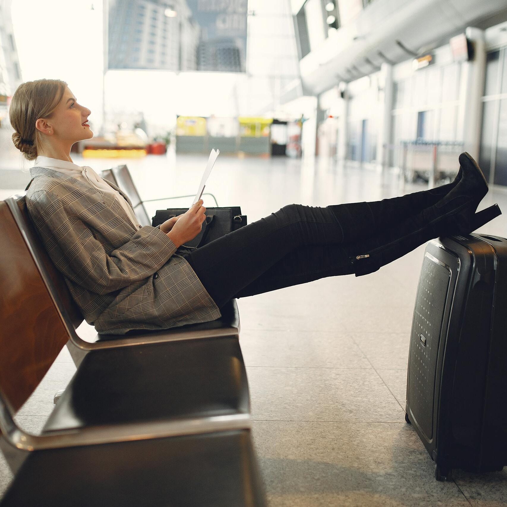 A woman relaxes in an airport terminal waiting area, reading a tablet with luggage nearby.