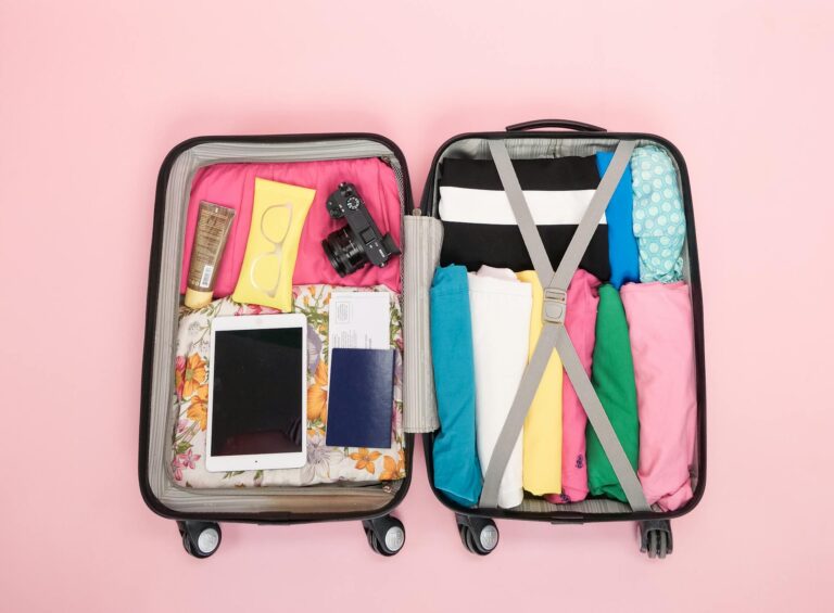 Open suitcase with travel essentials neatly packed on a pink backdrop. Perfect for vacation planning.