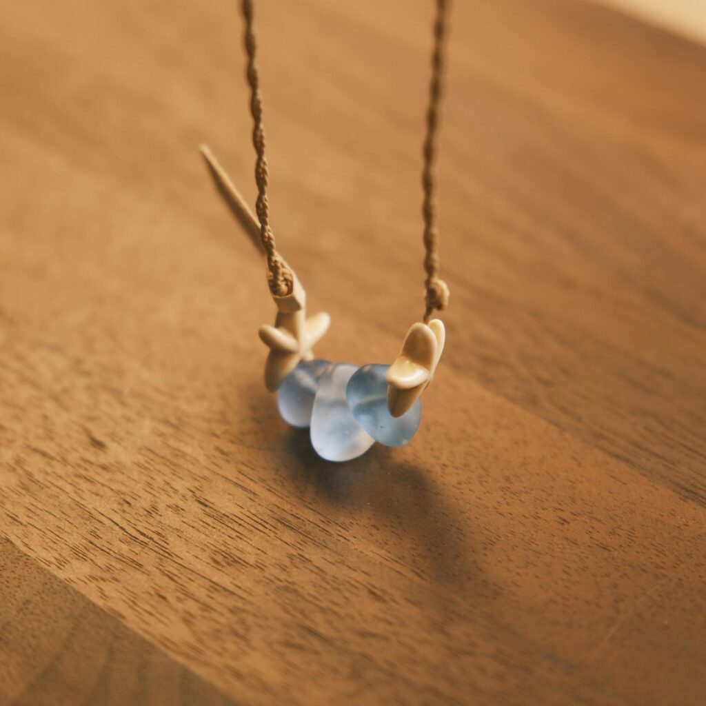 A beautiful handmade necklace featuring blue sea glass and shells on a wooden table, captured in soft light.