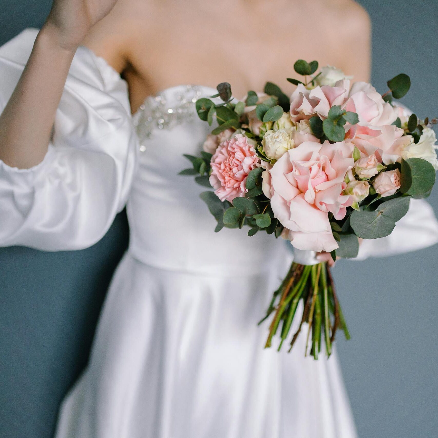 A bride in a white dress holding a bouquet of pink and white flowers against a blue background.