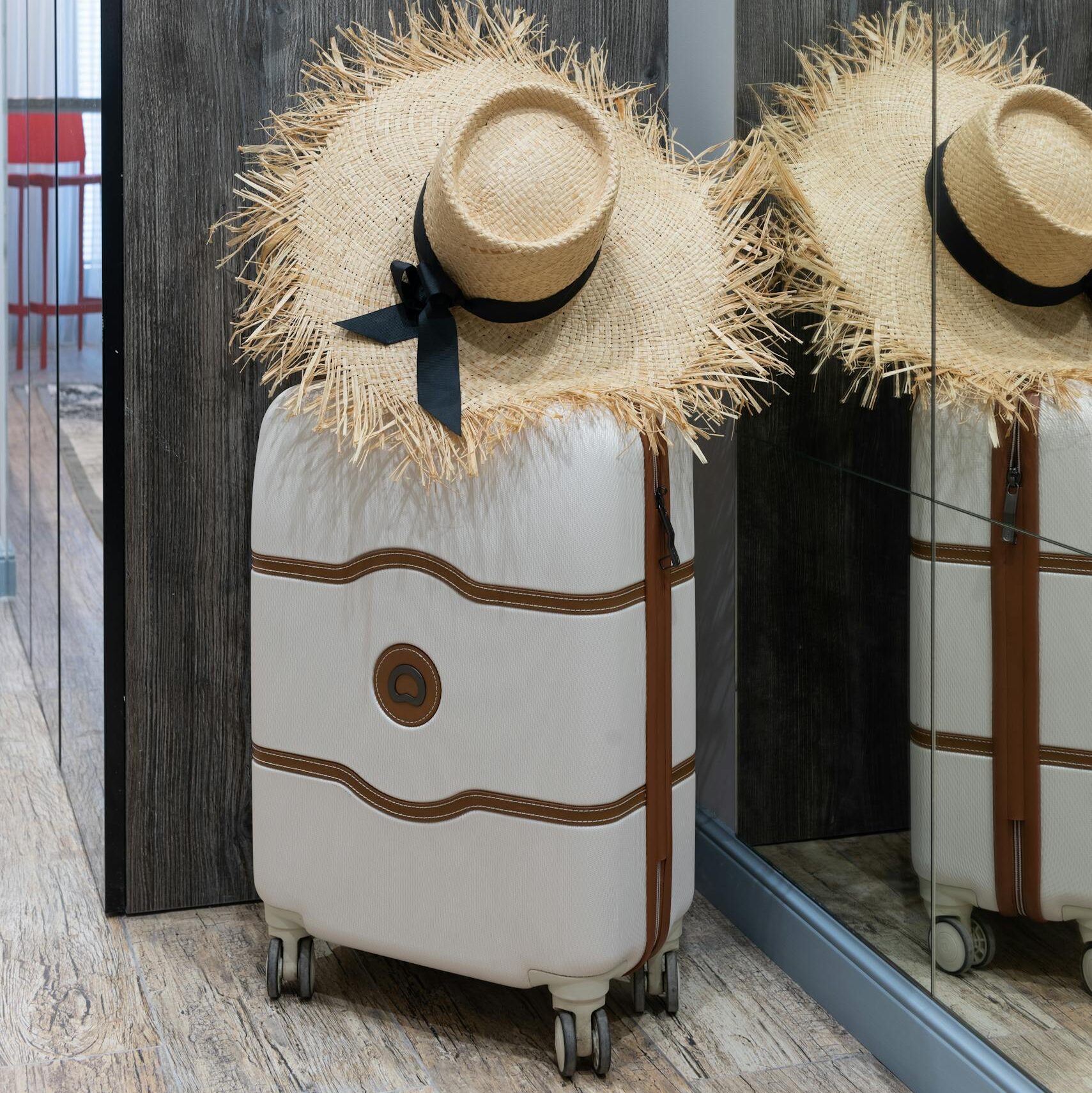 A chic straw hat resting on a suitcase in a contemporary hotel hallway, ready for travel.