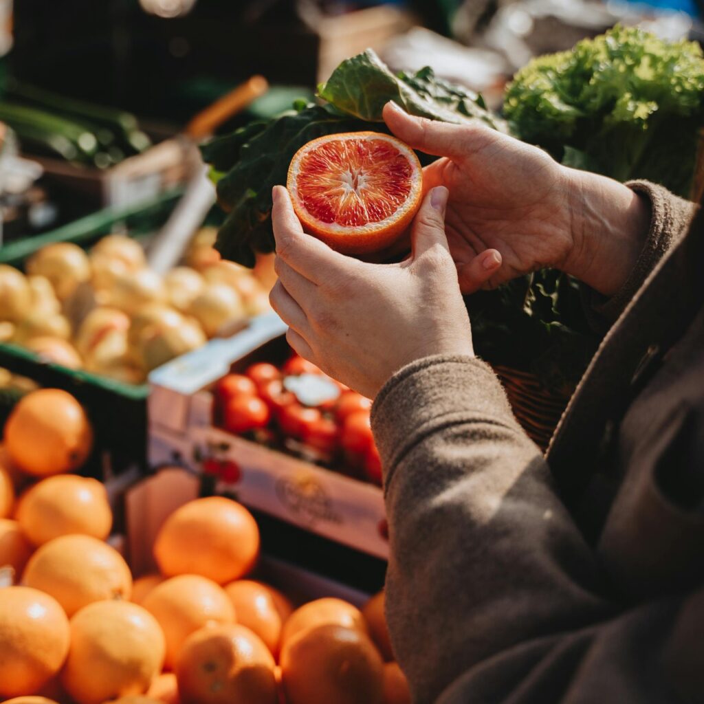 A close-up of a person holding a sliced orange at an outdoor market, showcasing fresh produce.