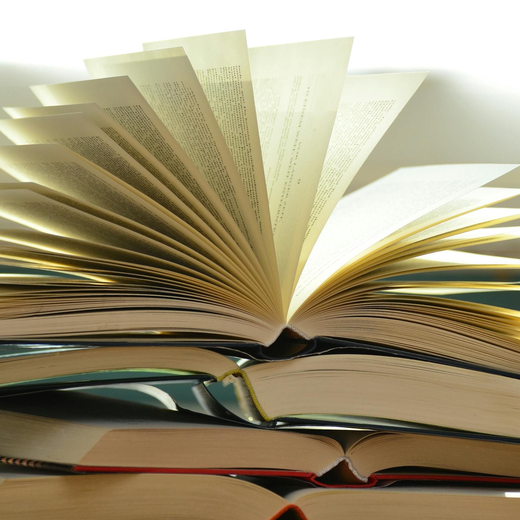 A close-up of a stack of open books with pages fanned out, capturing a study atmosphere.