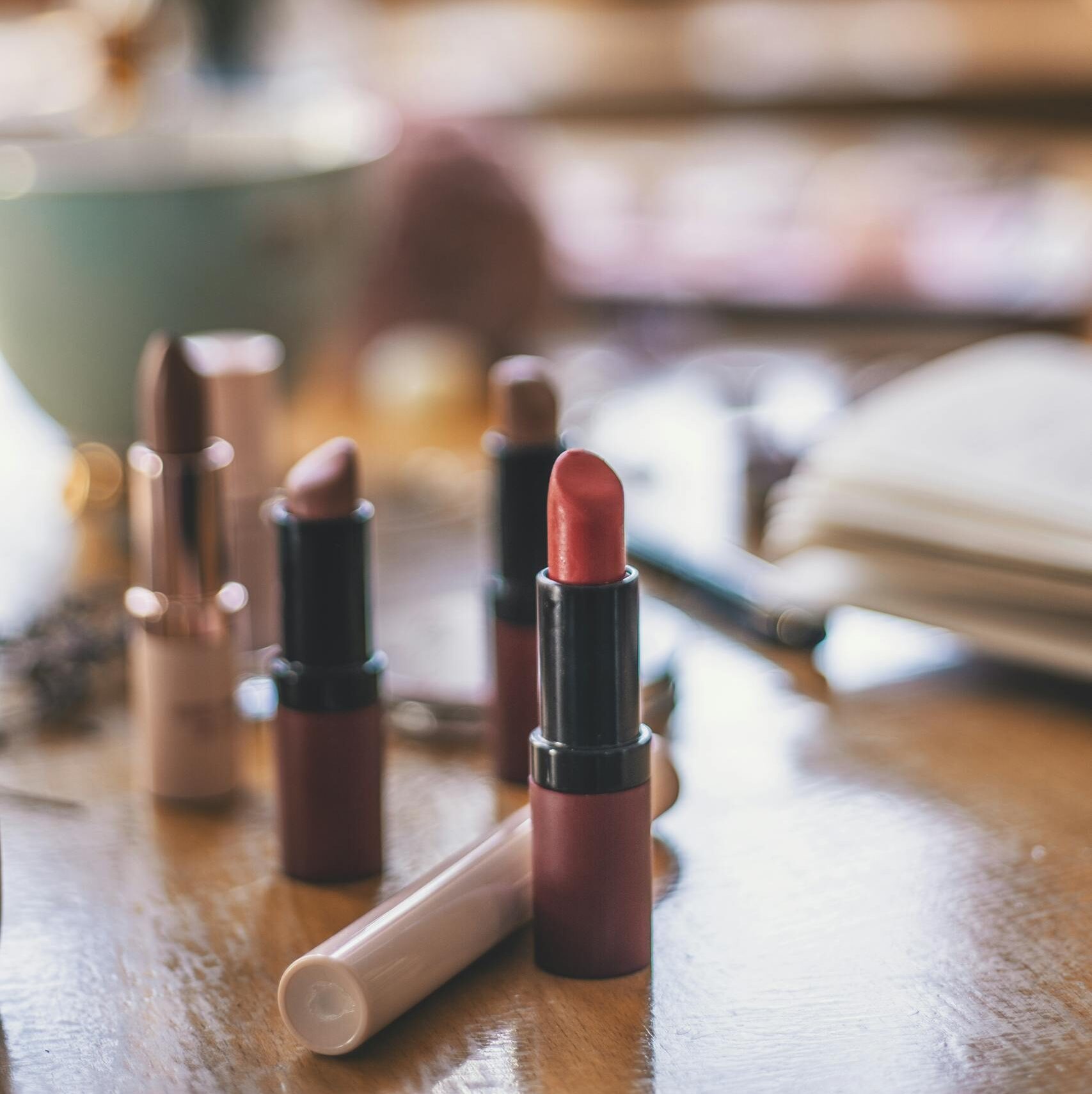 A close-up view of various lipsticks on a wooden table with a blurred background, emphasizing warmth and elegance.