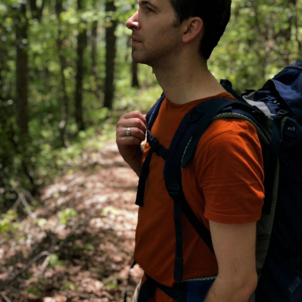 A man hiking in a lush green forest during daytime, carrying a backpack.