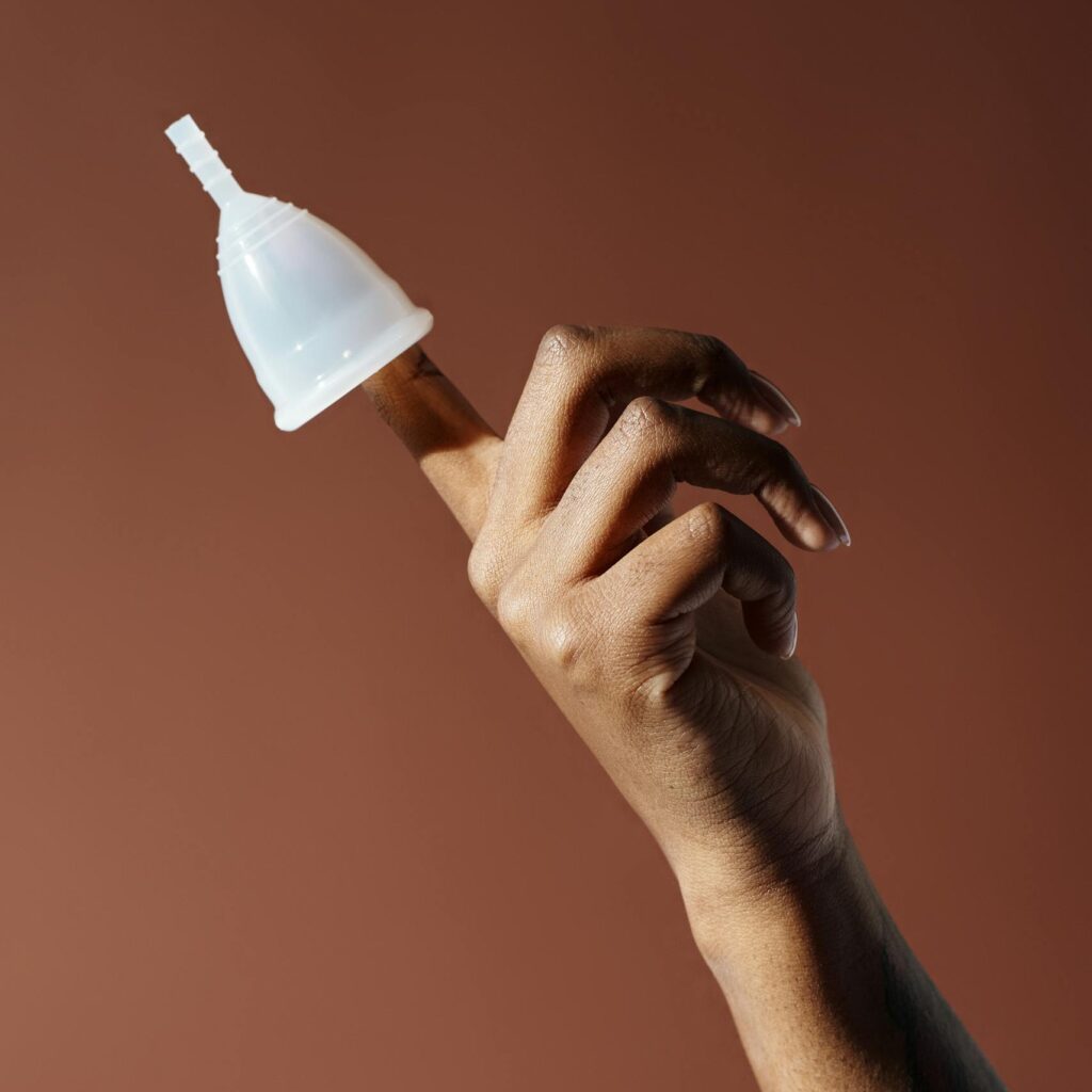 A menstrual cup balanced on a finger against a brown background, symbolizing eco-friendly menstrual care.