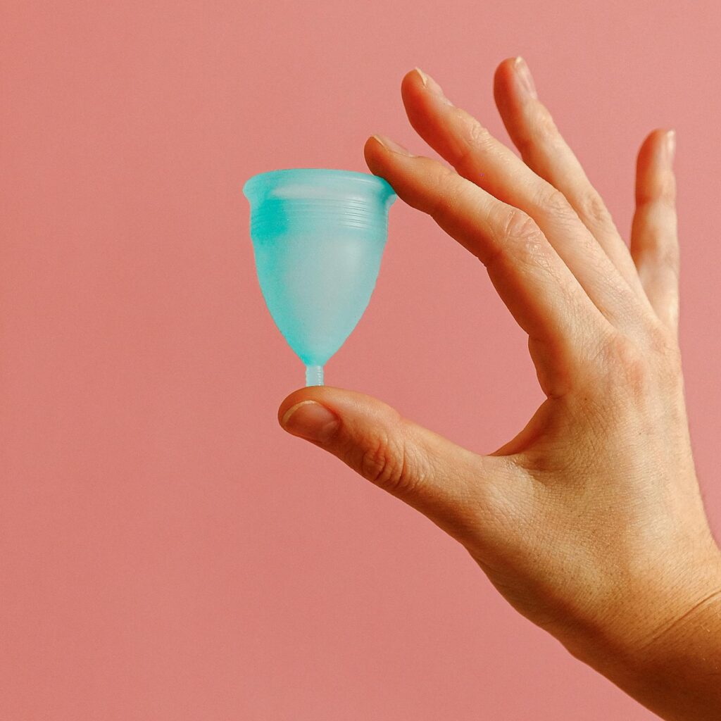 A reusable menstrual cup in a hand against a soft pink background, promoting eco-friendly feminine hygiene.