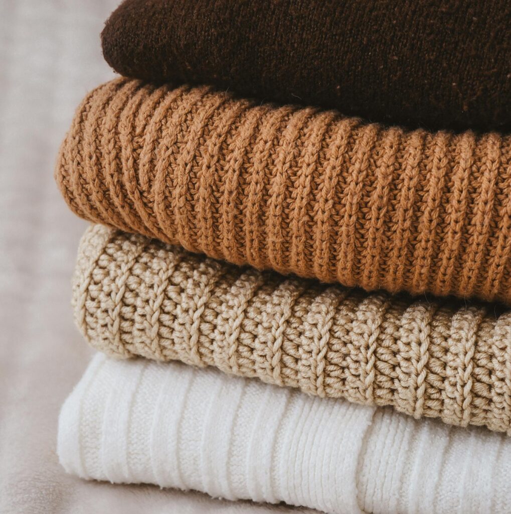 A stack of warm knitted sweaters in earthy tones, perfect for cozy winter days.