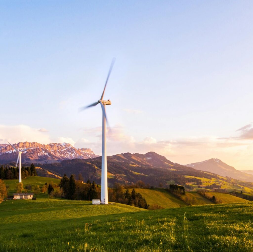 A wind turbine stands tall against a mountainous backdrop under a vibrant sky at sunset.