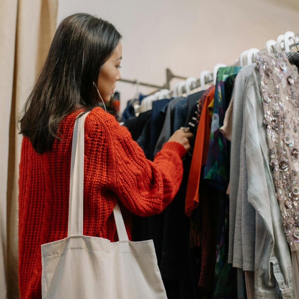 A woman browses a clothing rack in a cozy thrift shop, selecting garments.