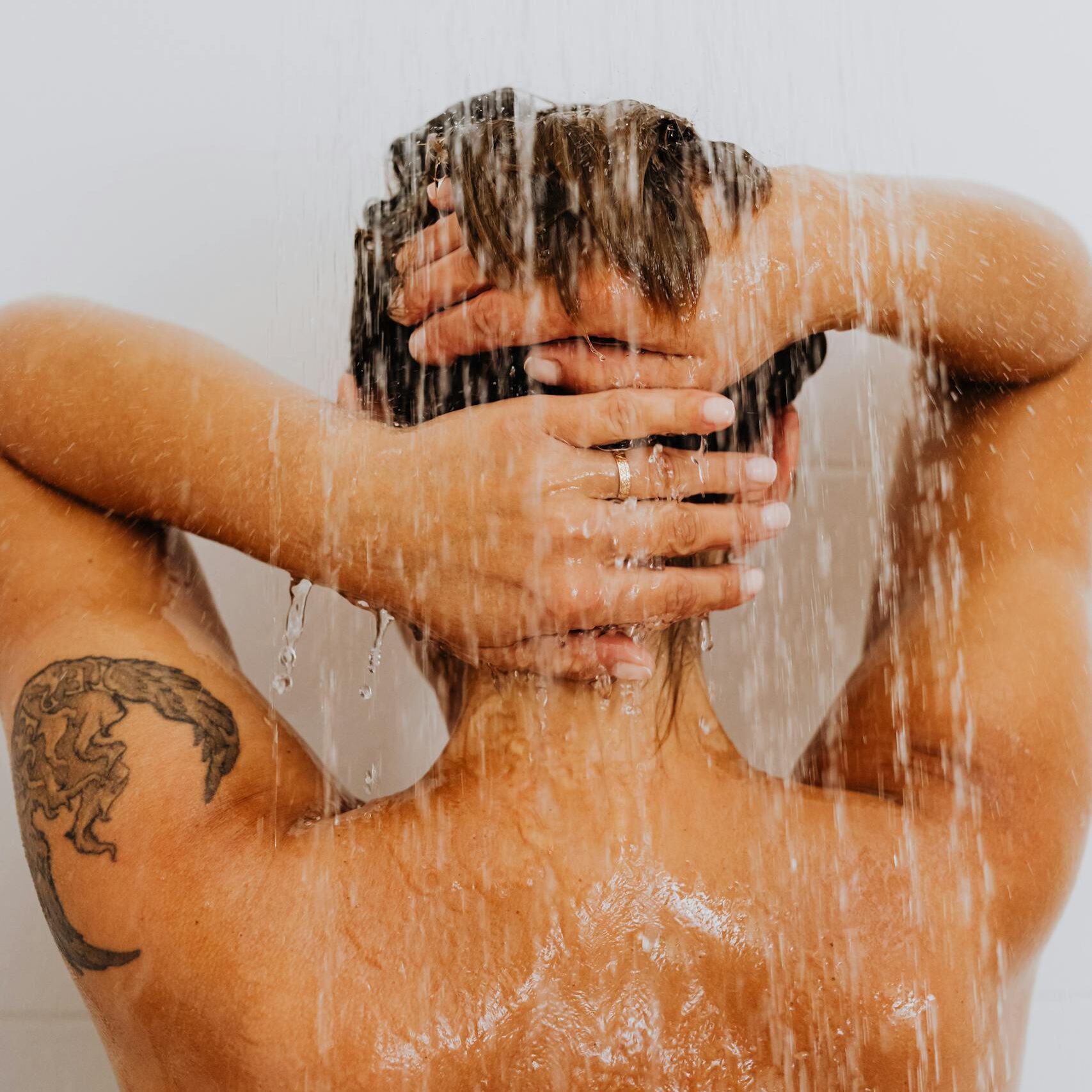 A woman with a tattoo enjoys a refreshing shower, symbolizing cleanliness and relaxation.