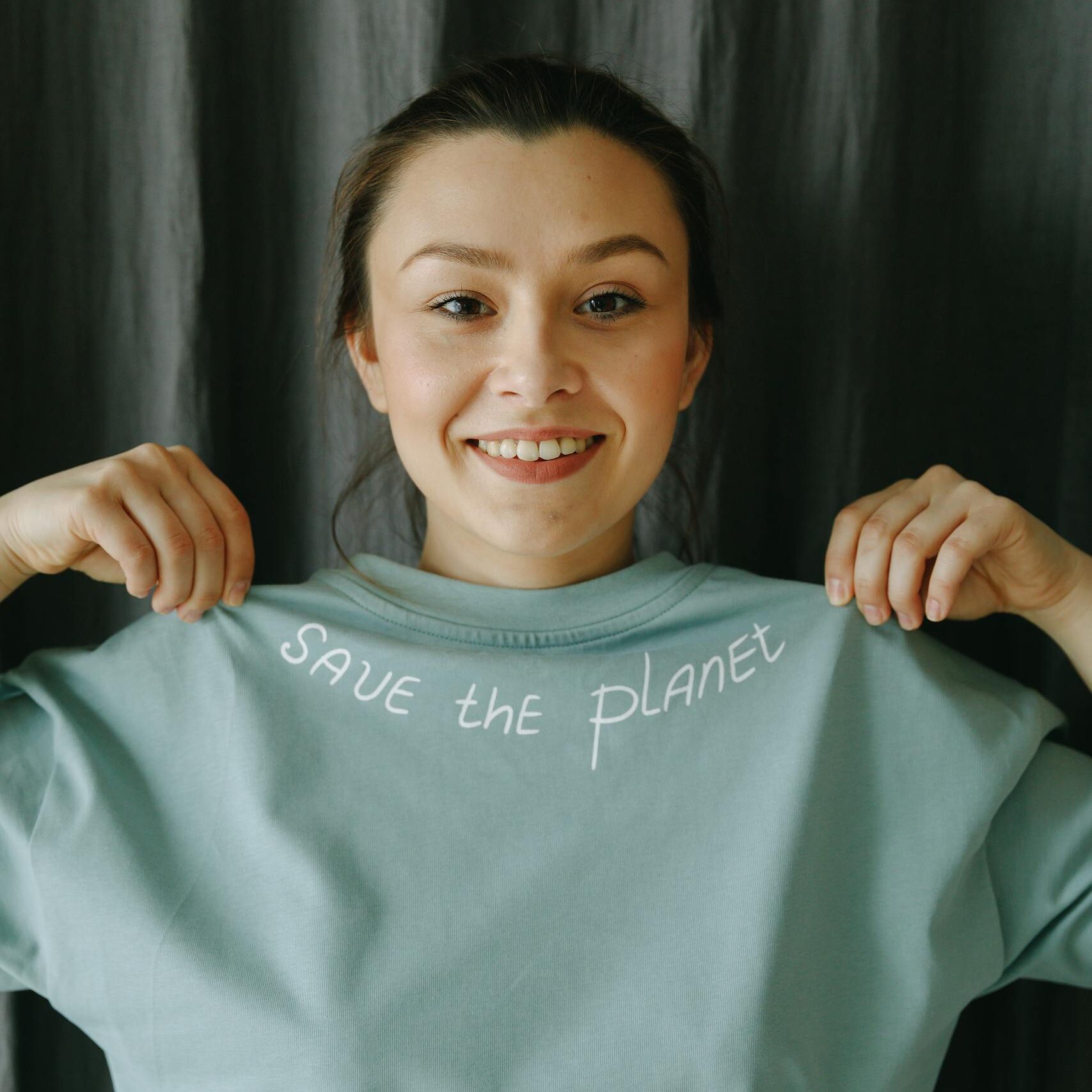 A young woman smiling while holding a 'Save the Planet' t-shirt, advocating environmental awareness.