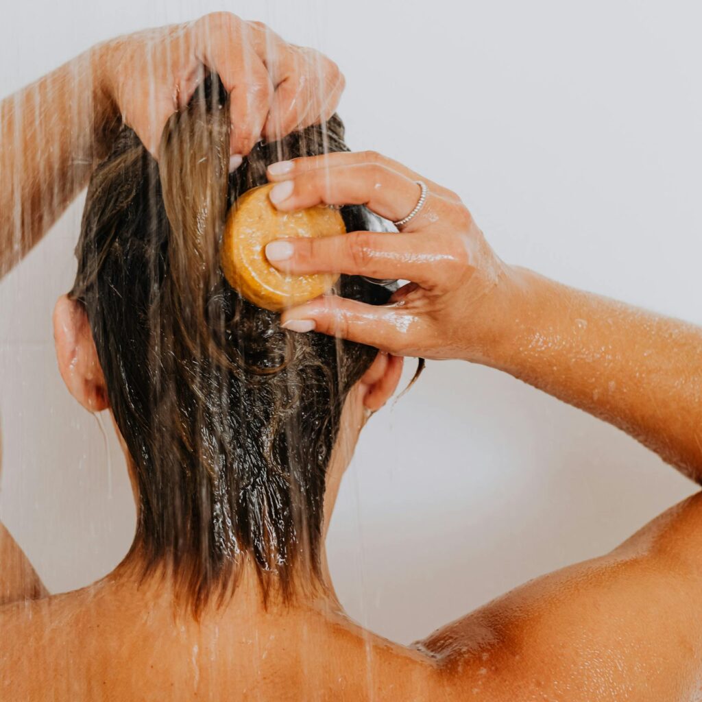Back view of a woman washing her hair in the shower under running water.