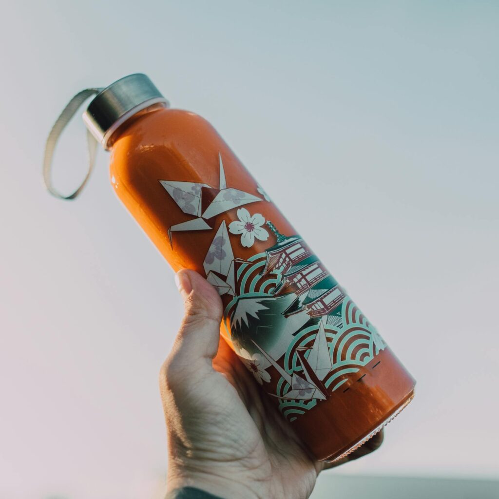 Close-up of a hand holding a decorative reusable water bottle against a clear sky.