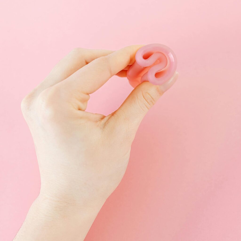 Close-up of a hand holding a folded menstrual cup against a pink background.