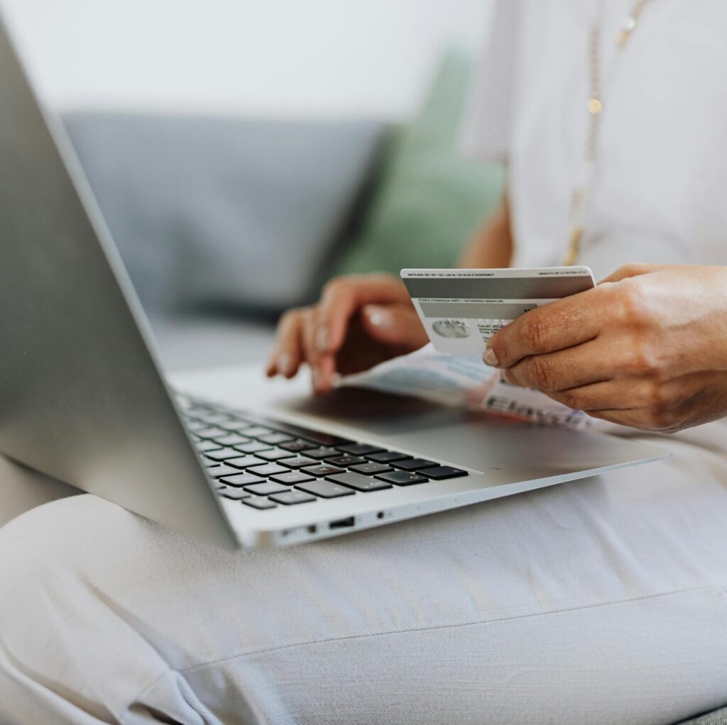 Close-up of a person holding a credit card while shopping online using a laptop at home.