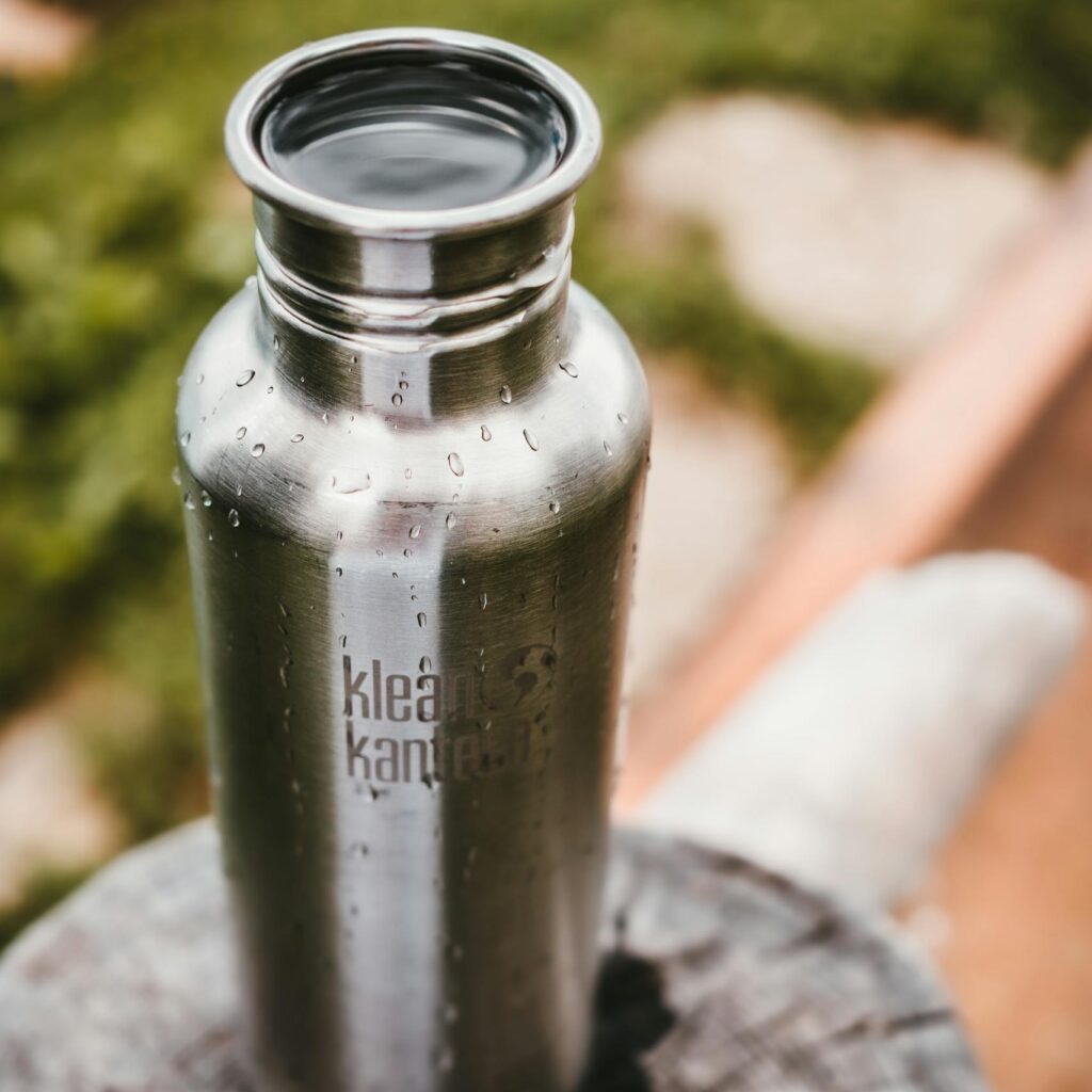 Close-up of a stainless steel water bottle on a wooden surface in a natural setting.