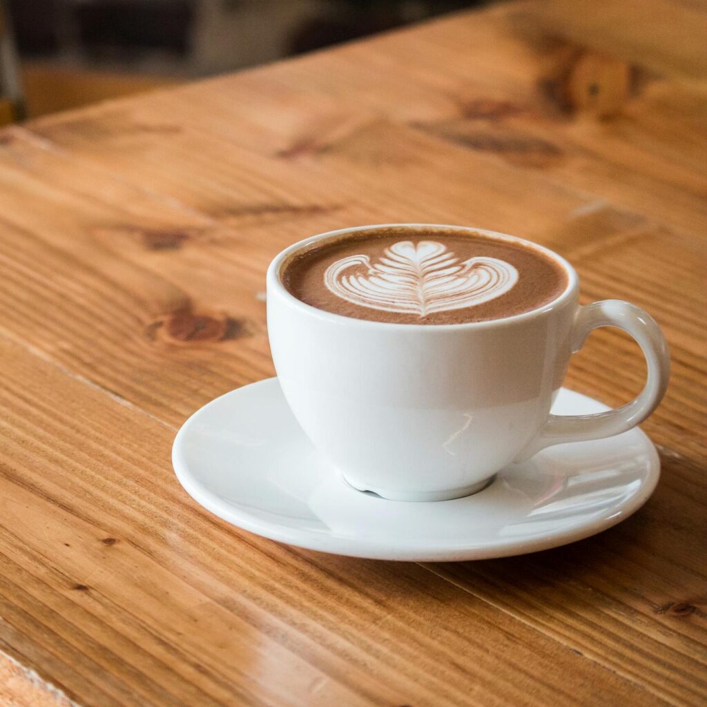 Close-up of a white cup of latte with artistic foam on a rustic wooden table.