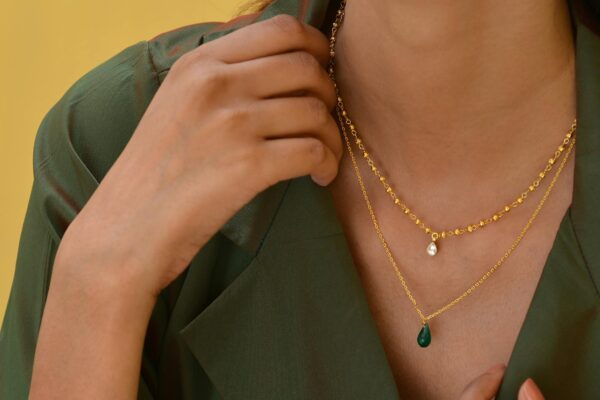 Close-up of a woman showcasing a stylish gold necklace against a green outfit and yellow background.