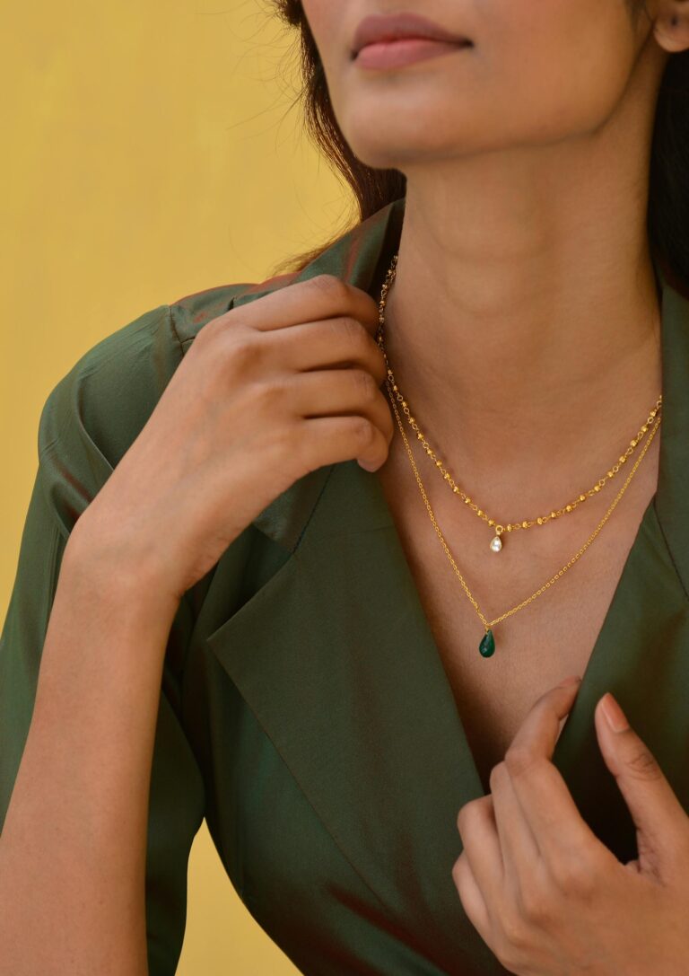 Close-up of a woman showcasing a stylish gold necklace against a green outfit and yellow background.