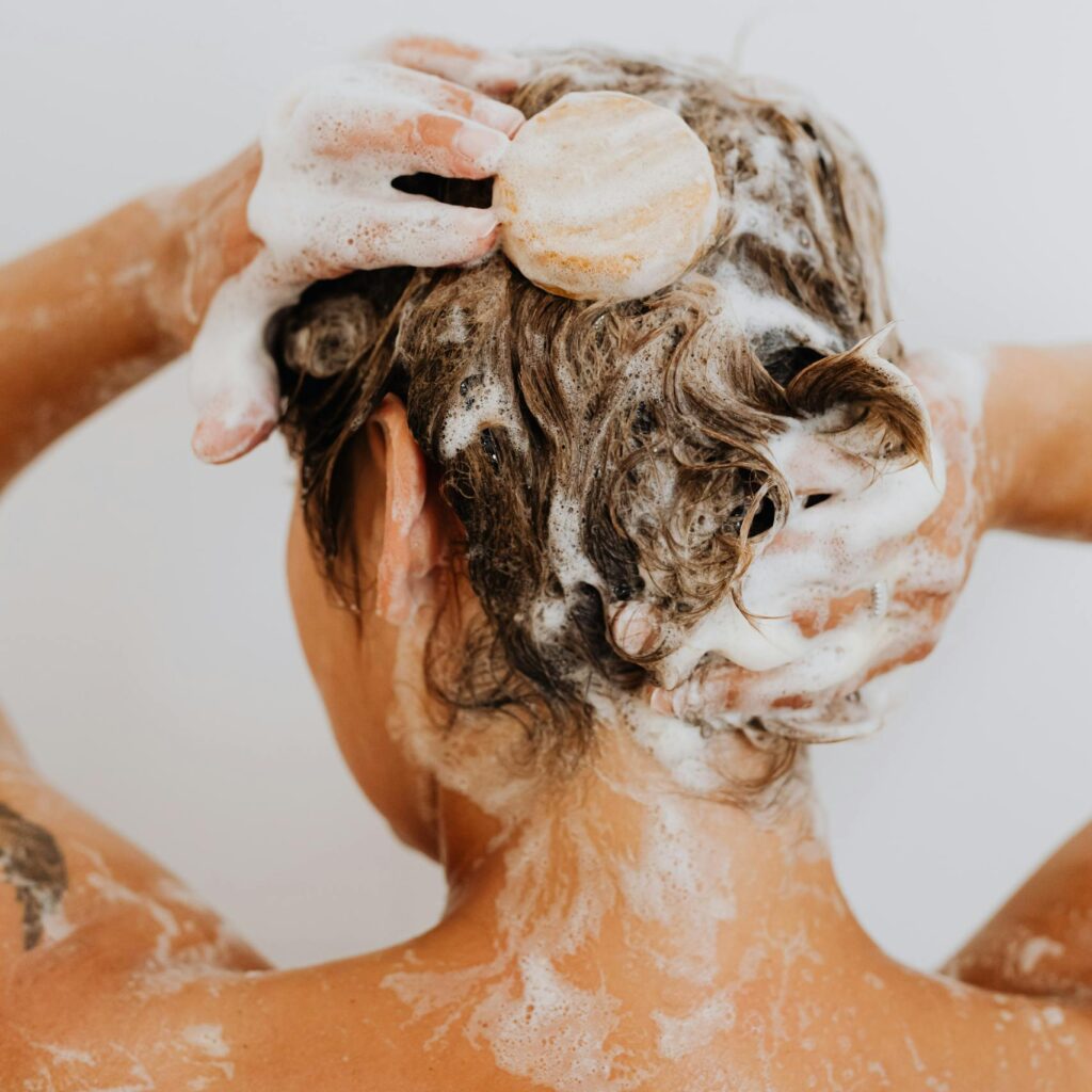 Close-up of a woman washing her hair with soap and lather in the shower.