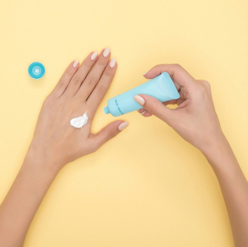 Close-up of a woman's hands applying cream on a pastel yellow background. Ideal for beauty and skincare themes.