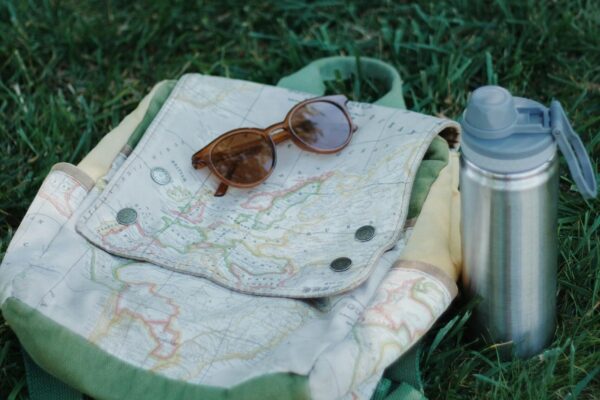 Close-up of backpack, sunglasses, and thermos on grass, perfect for travel and exploration.