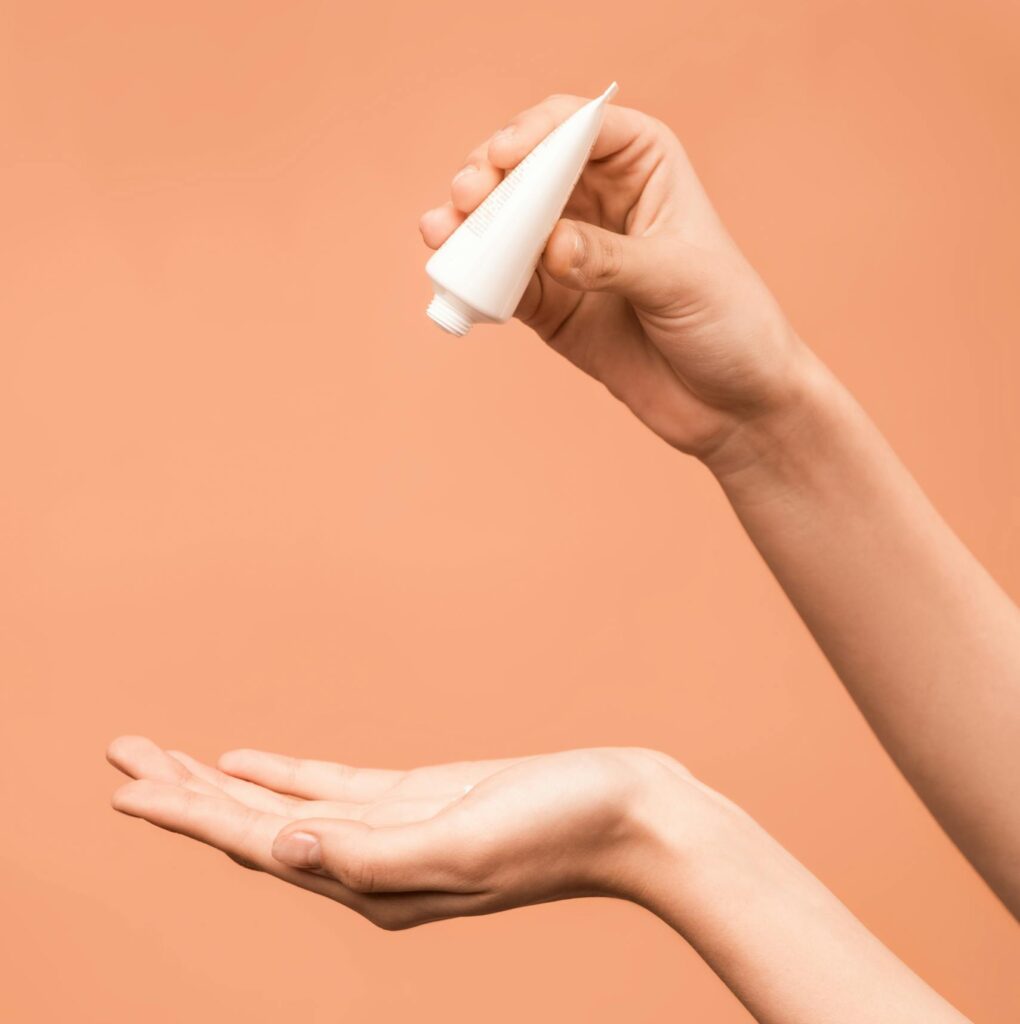 Close-up of hands applying lotion from a tube against a peach background.
