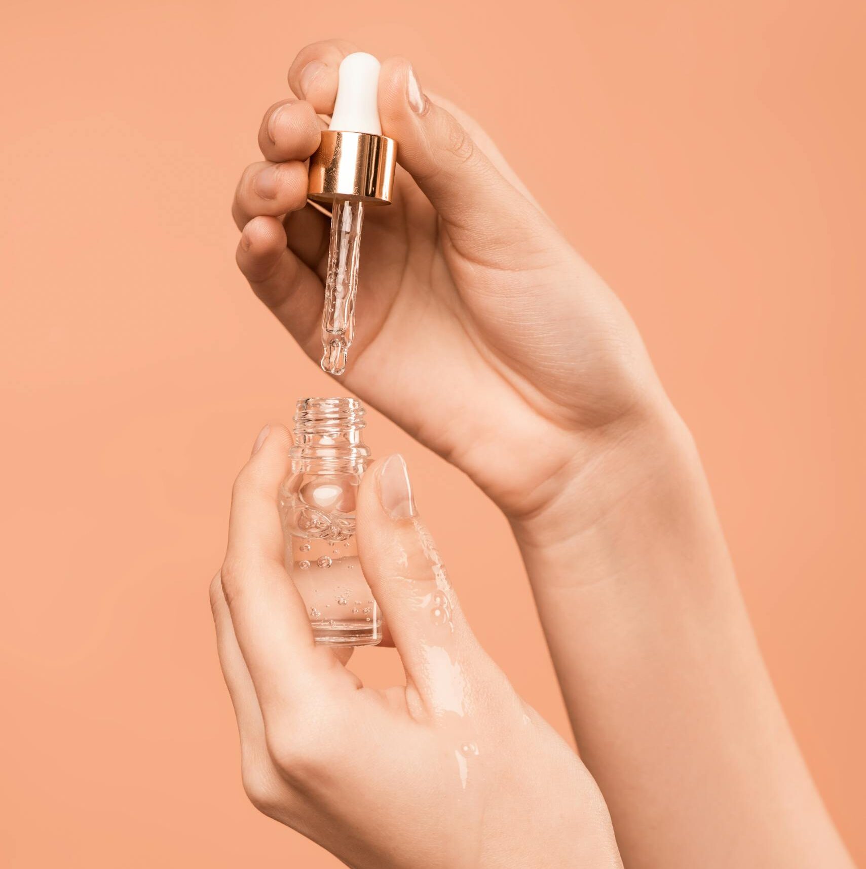 Close-up of hands using a dropper to apply skincare serum, ideal for health and beauty content.