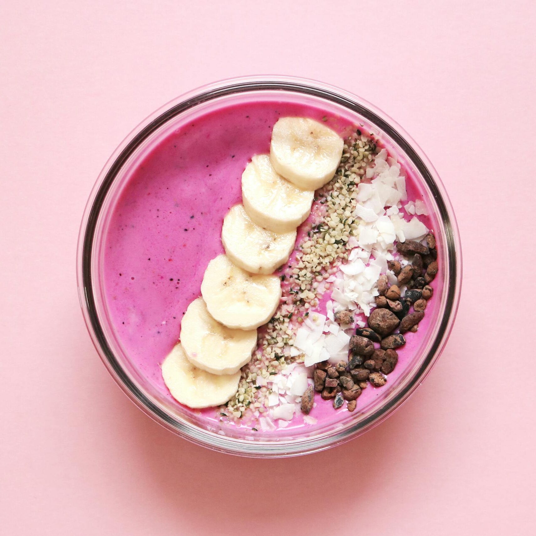 Colorful açaí smoothie bowl with banana, chia seeds, and more on pink background.
