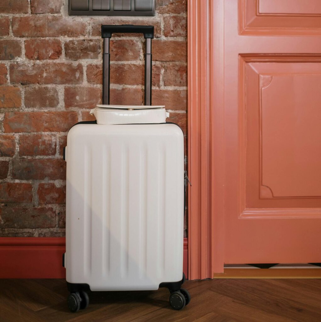 Compact white suitcase against a rustic brick wall beside a coral door, perfect for travel themes.
