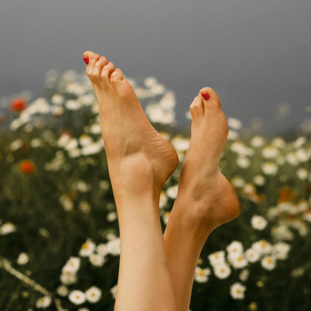 Feet with red pedicure among chamomile flowers in Belarus, symbolizing relaxation and nature.