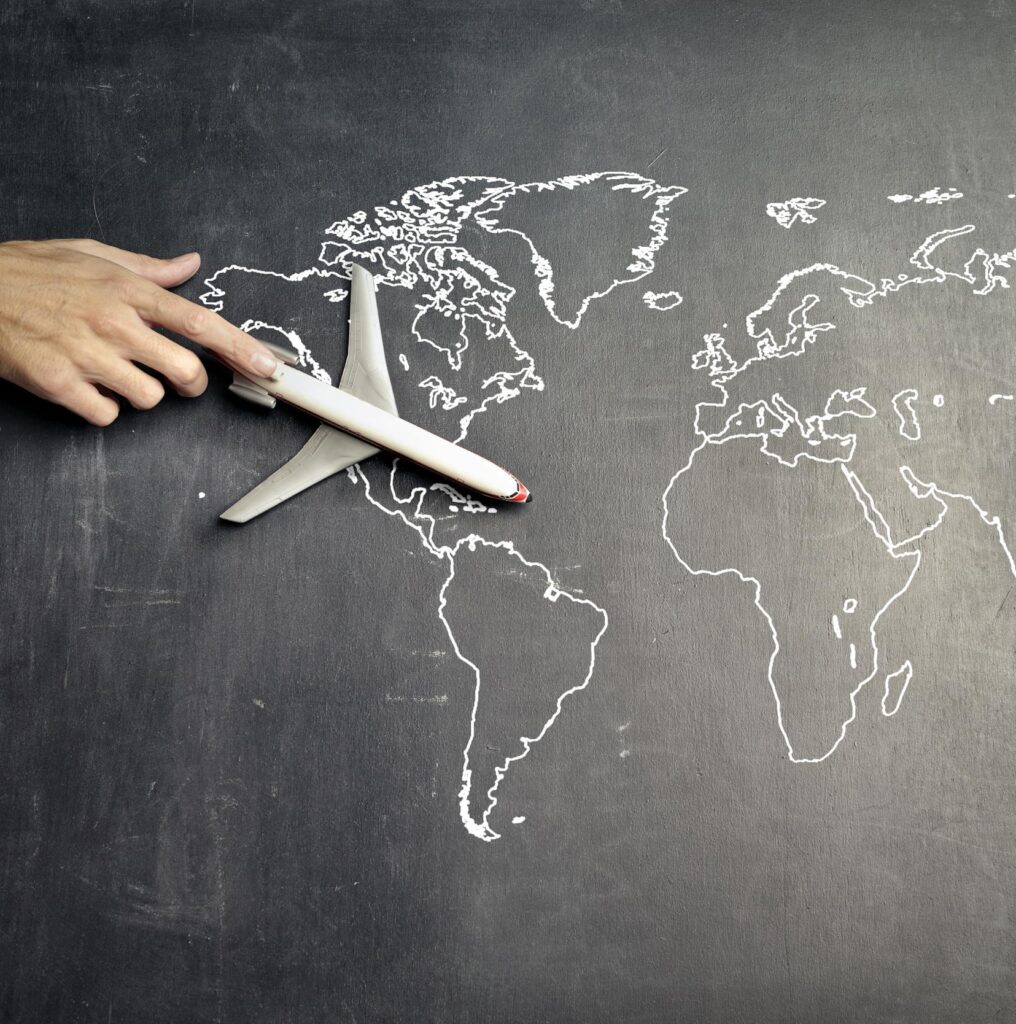 From above of crop anonymous person driving toy airplane on empty world map drawn on blackboard representing travel concept