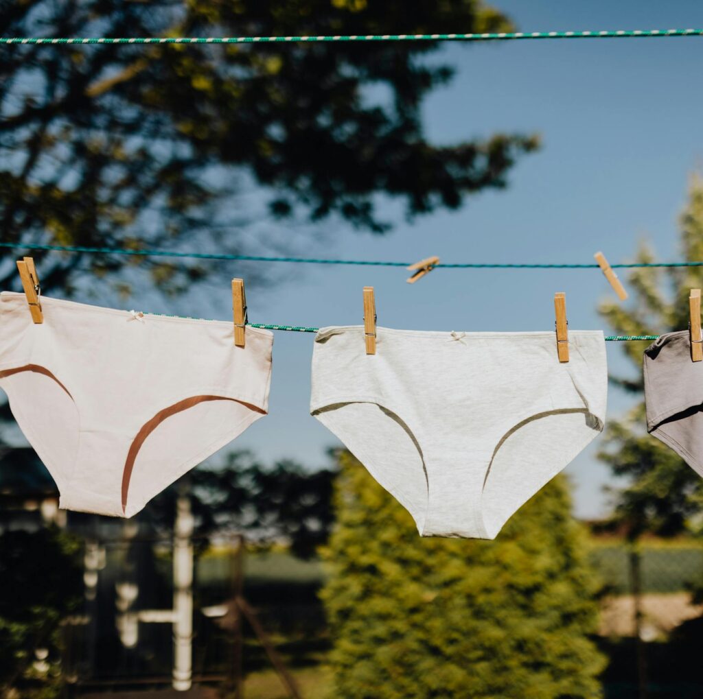 From below of washed feminine underwear hanging on rope with clothespins outdoors on sunny summer weather against blue sky and green trees