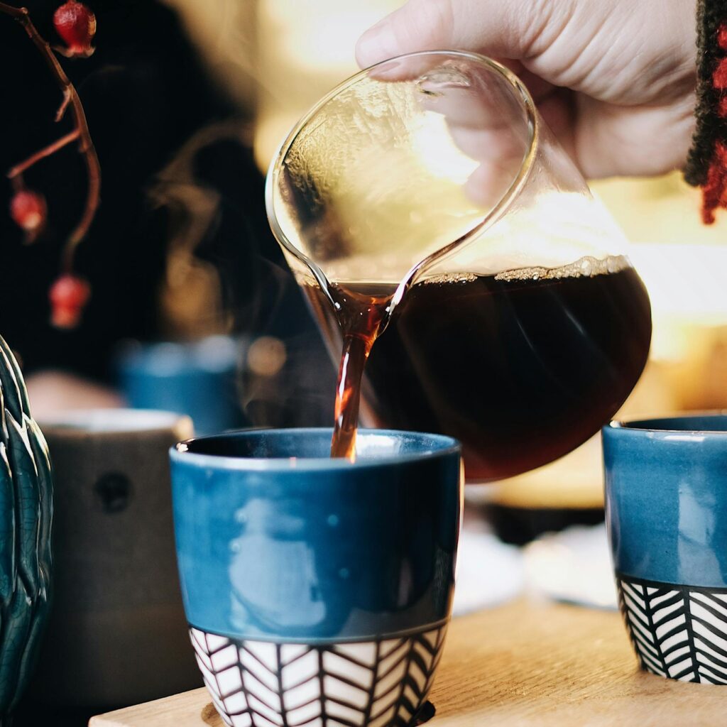 Hand pouring hot coffee into a blue ceramic cup, creating a cozy indoor vibe.