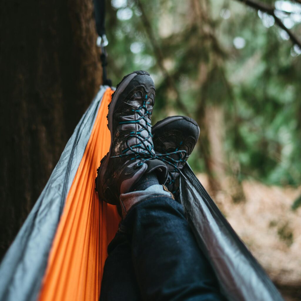 Man relaxing in a hammock with boots in a serene forest setting, ideal for adventure and travel themes.