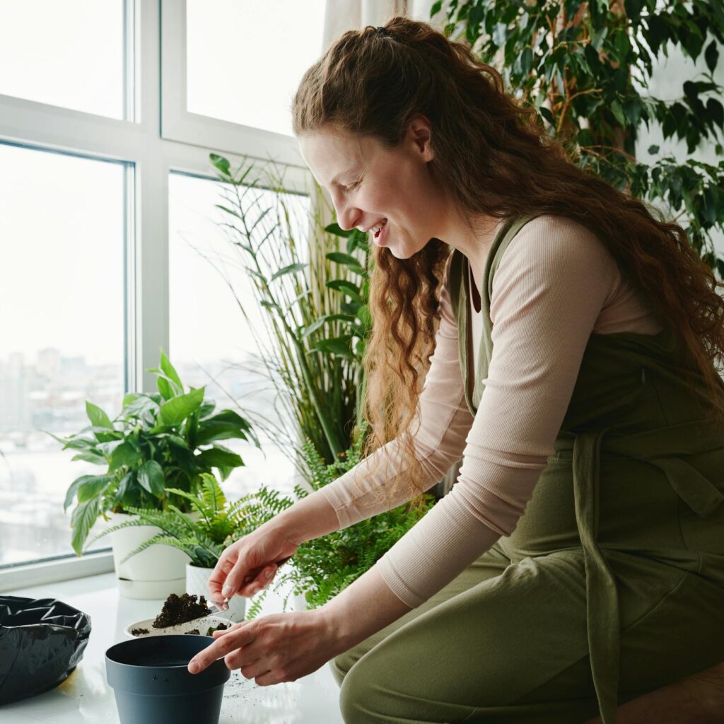 Pregnant woman planting indoors with trowel, surrounded by green plants.