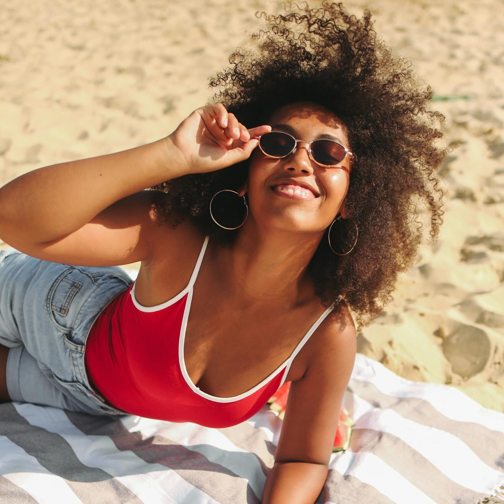Smiling woman enjoying sunny day on the beach with sunglasses and striped towel.