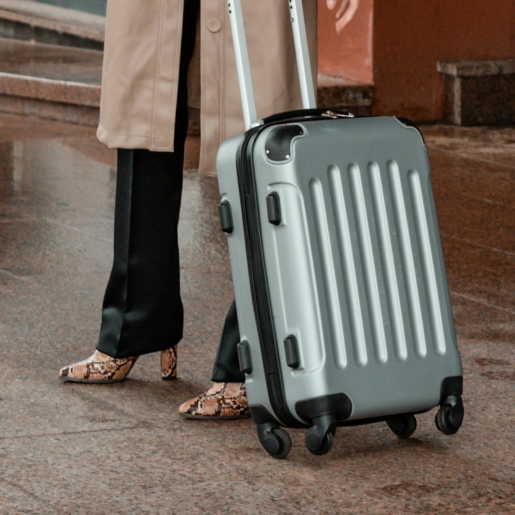 Stylish traveler in a trench coat holding a suitcase at an airport terminal.