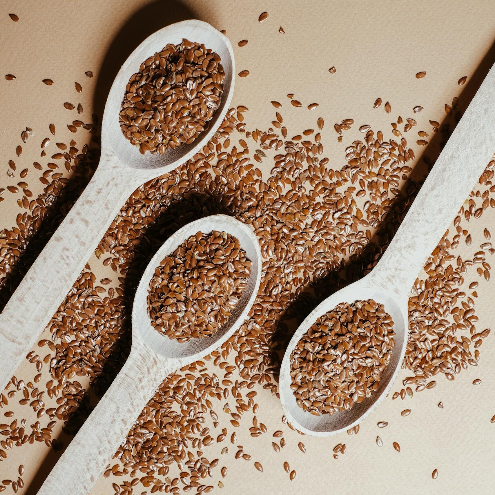 Three wooden spoons filled with flaxseeds on a table, showcasing healthy organic ingredients.