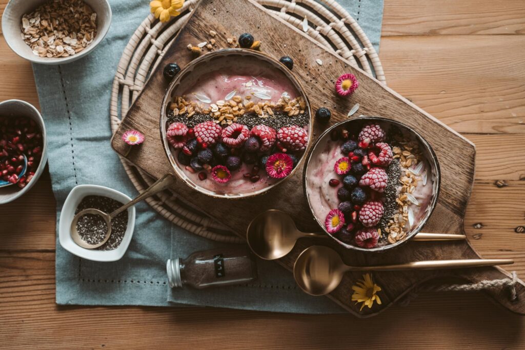 Top view of berry smoothie bowls with granola on a rustic wooden board, perfect vegan breakfast.