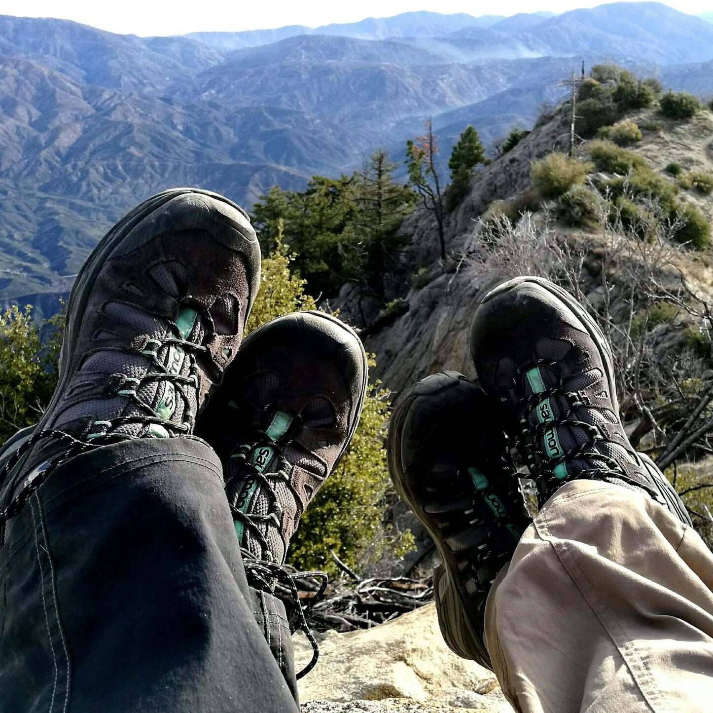 Two hikers resting with boots in view, overlooking a scenic mountain landscape.
