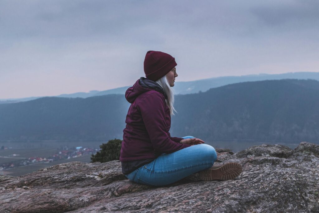 Woman sitting on a rock, enjoying the serene mountain view.