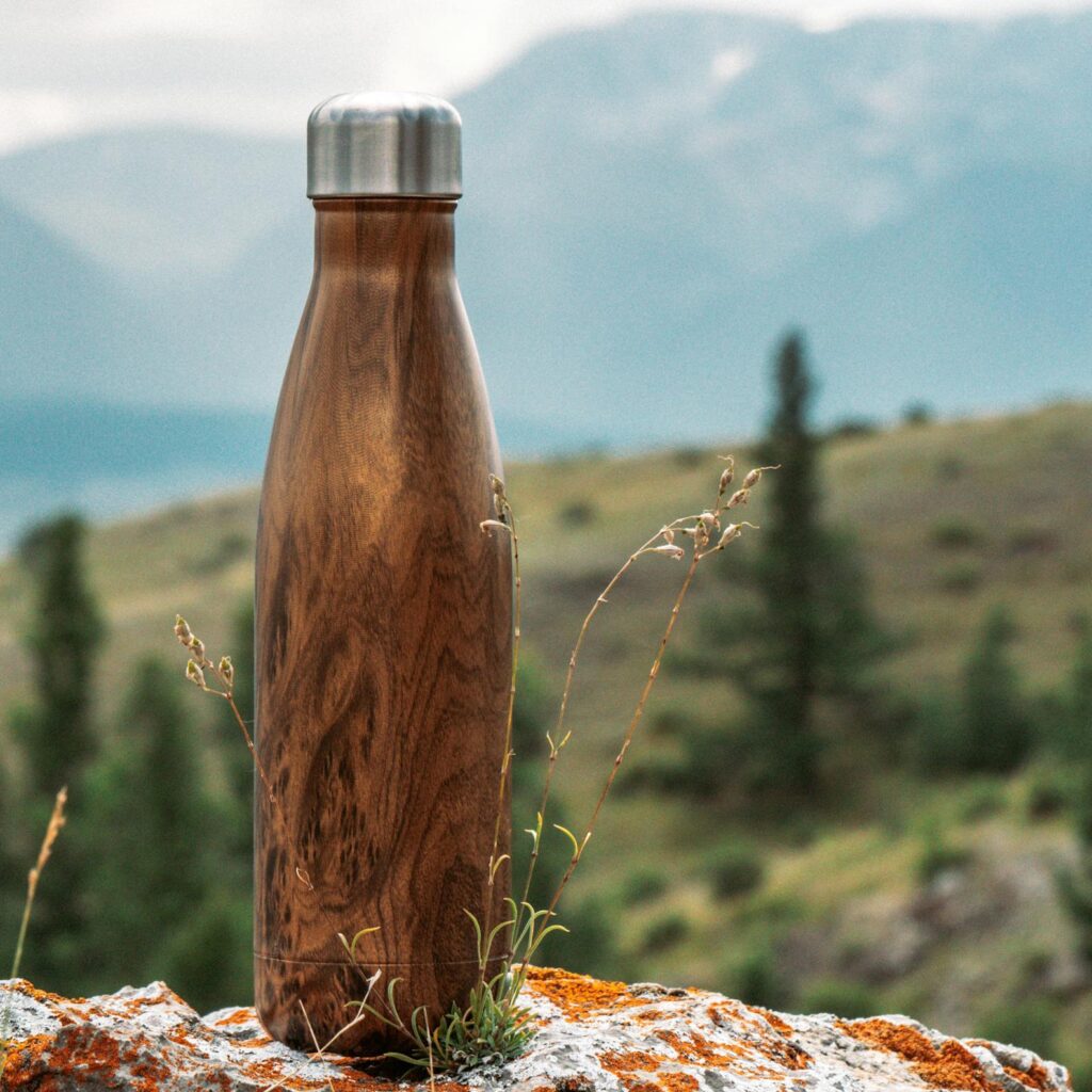 Wood grain water bottle on a rocky surface with a mountainous backdrop, ideal for outdoor adventures.
