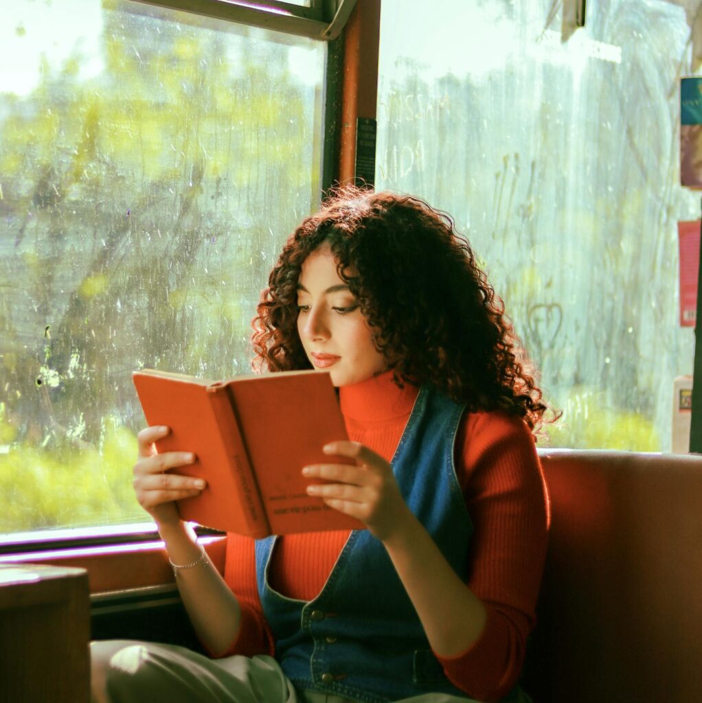 Young woman reading a book while traveling on a bus, bathed in natural light.